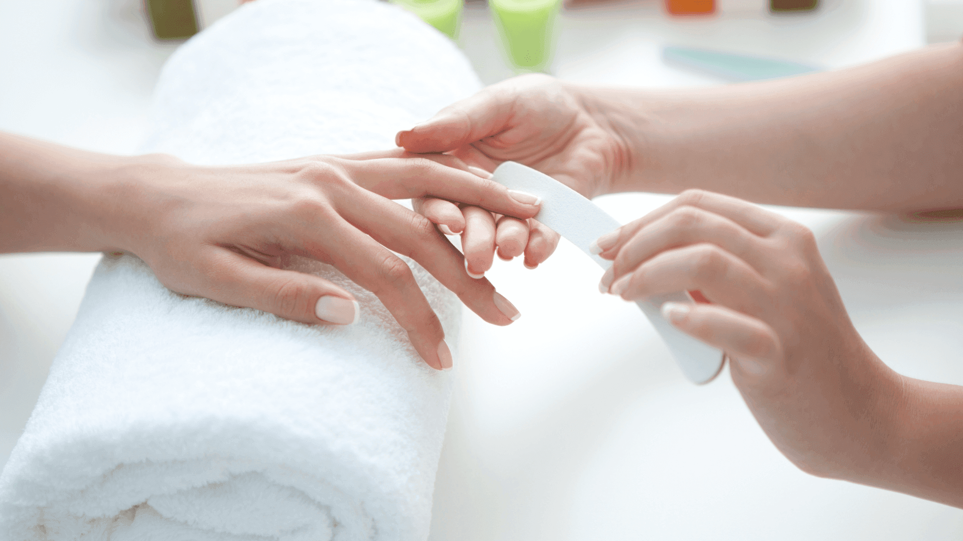 Manicure: l’operatrice lima le unghie di una cliente che appoggia la mano su un asciugamano arrotolato
