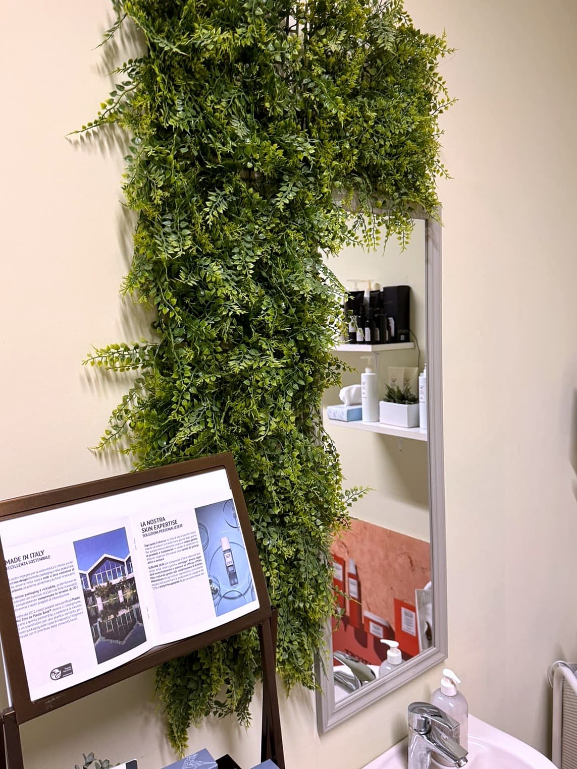 Angolo di Dova Estetica con una parete di foglie verdi accanto allo specchio, il lavabo e un leggio con il materiale informativo Comfort Zone