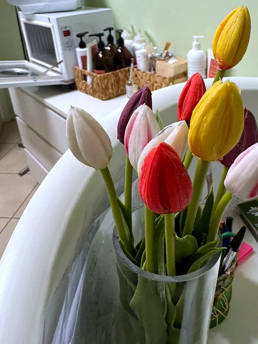 Tulipani rossi, gialli, bianchi e viola in un vaso di vetro sulla postazione di Dova Estetica, con i flaconi dei prodotti professionali sullo sfondo
