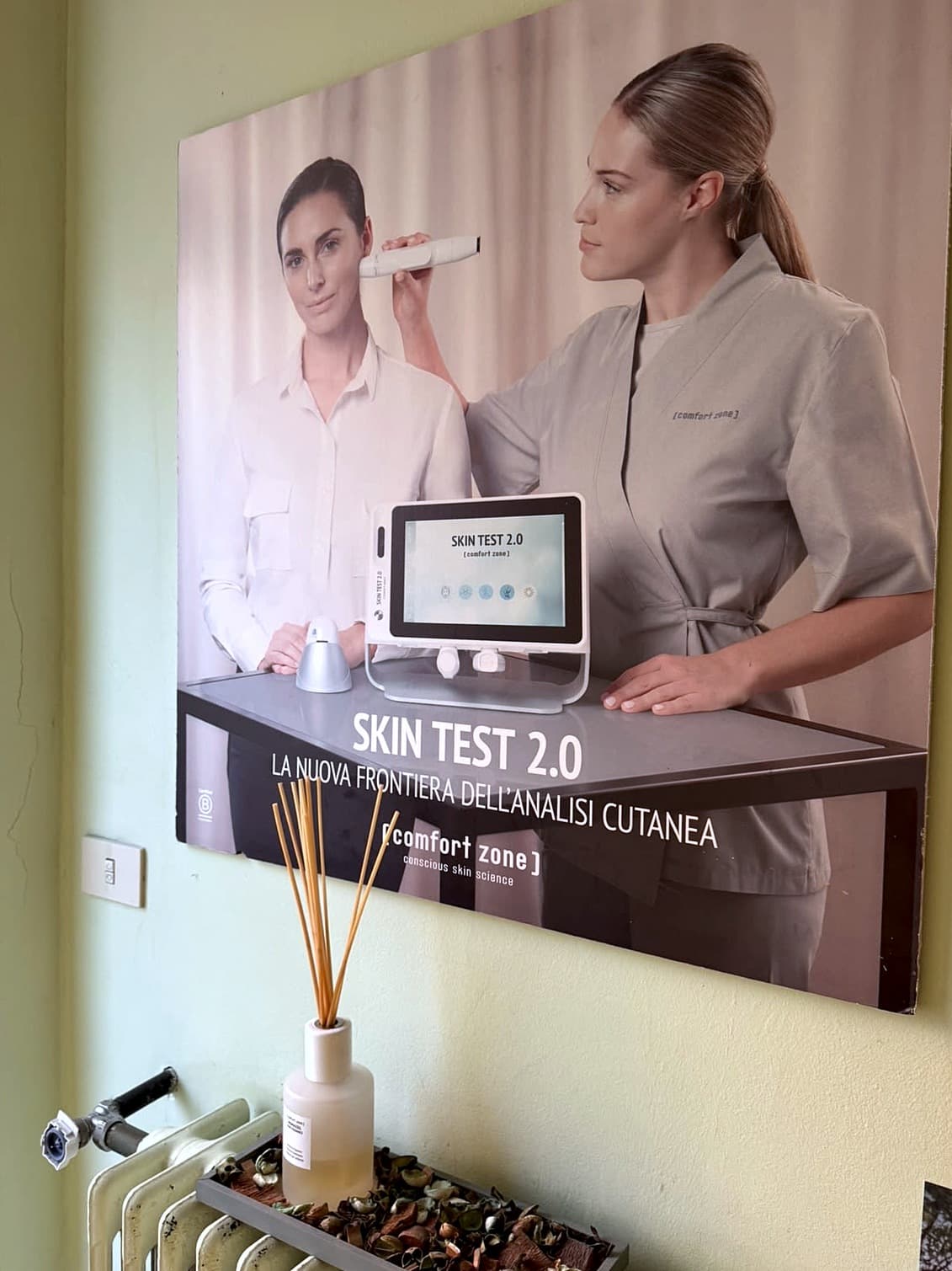 Poster Comfort Zone Skin Test 2.0, la nuova frontiera dell’analisi cutanea, appeso in Dova Estetica, con un’operatrice che analizza la pelle del viso di una cliente con il dispositivo