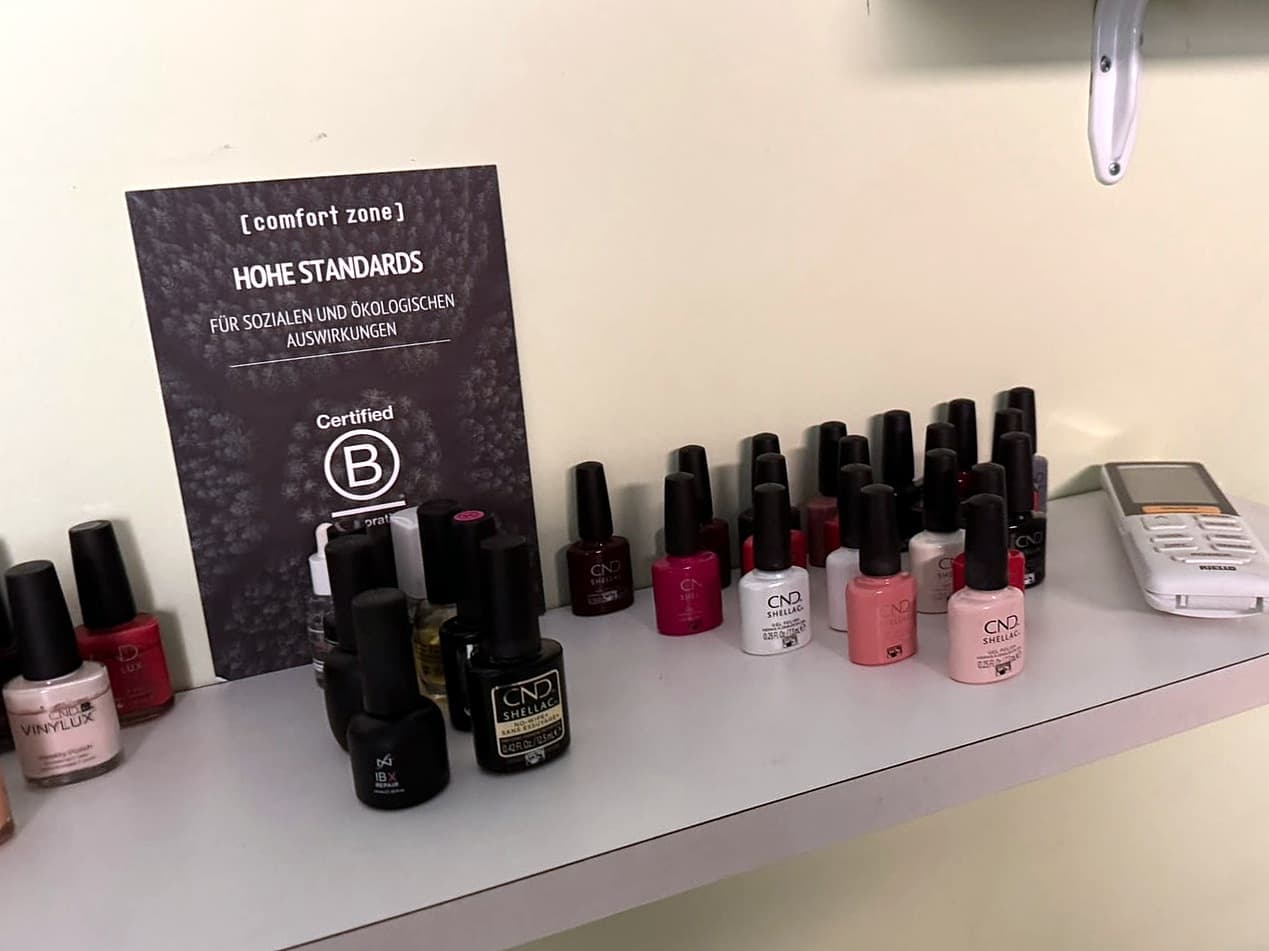 Smalti semipermanenti CND Shellac e Vinylux in fila sulla mensola di Dova Estetica, accanto al cartello Comfort Zone con il marchio Certified B Corporation