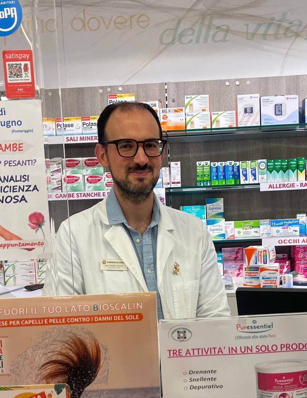 Daniele Facchi, farmacista, in camice bianco dietro il banco della farmacia