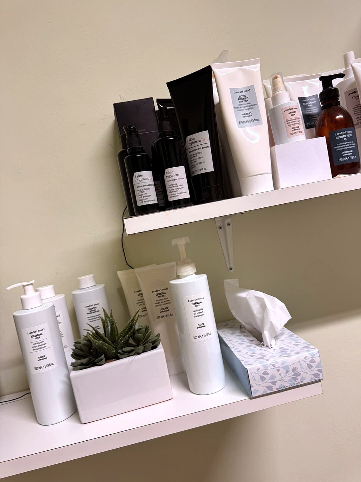 Mensole della cabina di Dova Estetica con i prodotti professionali Comfort Zone per il viso, tra cui latte detergente, tonico e peeling della linea Essential e la maschera Active Pureness